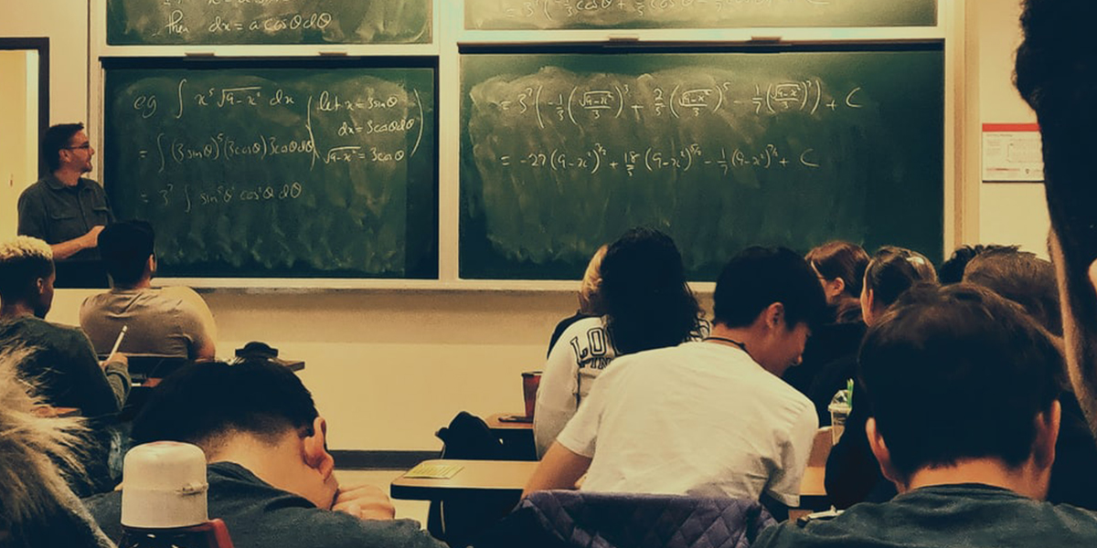 a classoom filled with students listening to a professor speak